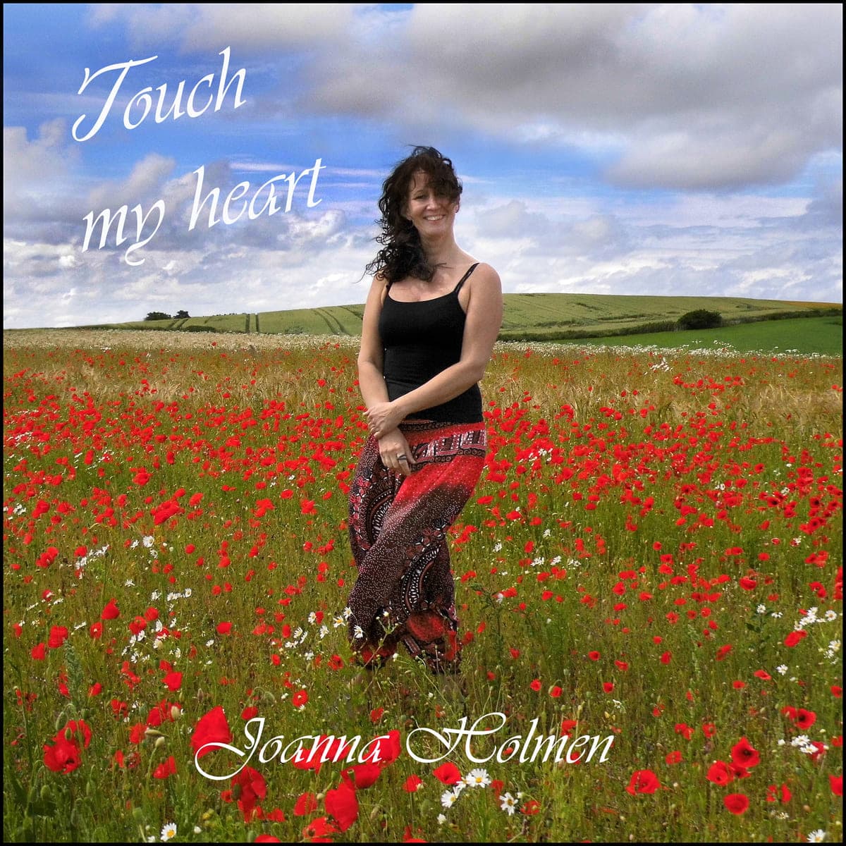 Joanna Holmen står smilende i en valmuemark under blå sommerhimmel. Cover til singlen Touch My Heart