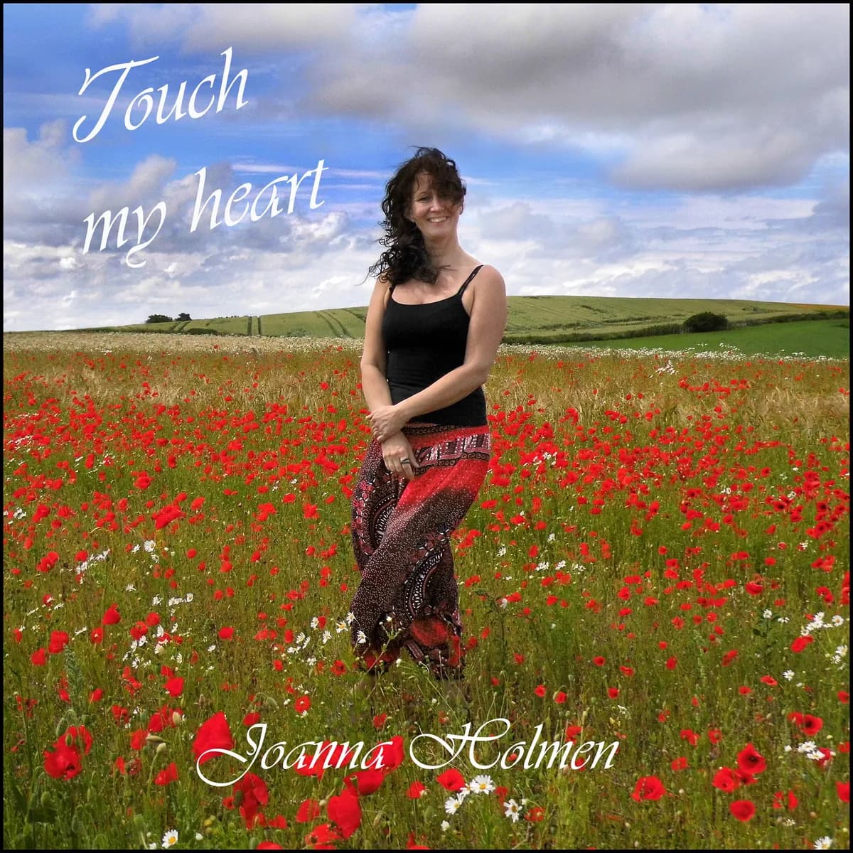Joanna Holmen står smilende i en valmuemark under blå sommerhimmel. Cover til singlen Touch My Heart